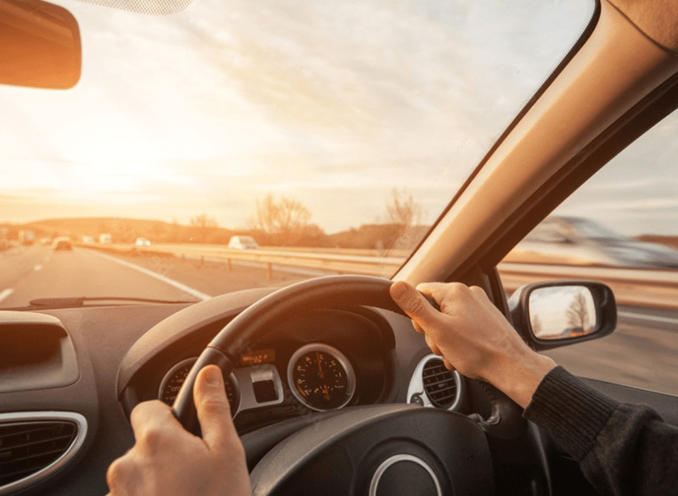 view of a drivers hand holding the steering wheel while viewing the road in front fron UNO Driving School.