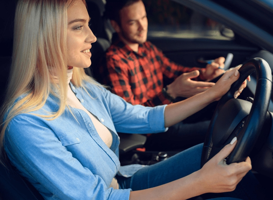 A driving student with a driving instructor in a car is learning to drive.
